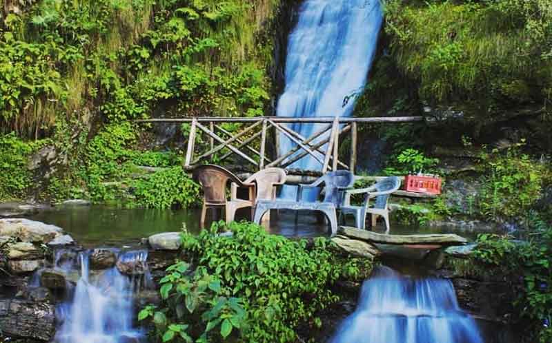 water falling from the top of mountain range and passing through the area surrounds with chairs and wooden bridge at Jana Waterfall