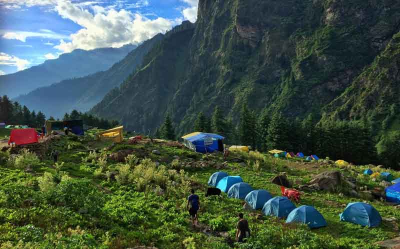 On the mountain lush greenery range, people camping around after trekking to the top of kheerganga peak to see the beautiful landscape.