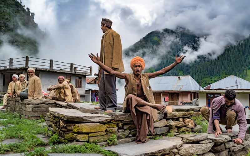 Fog around the malana village where people sitting and chilling by doing work and singing around with the mountain view. 